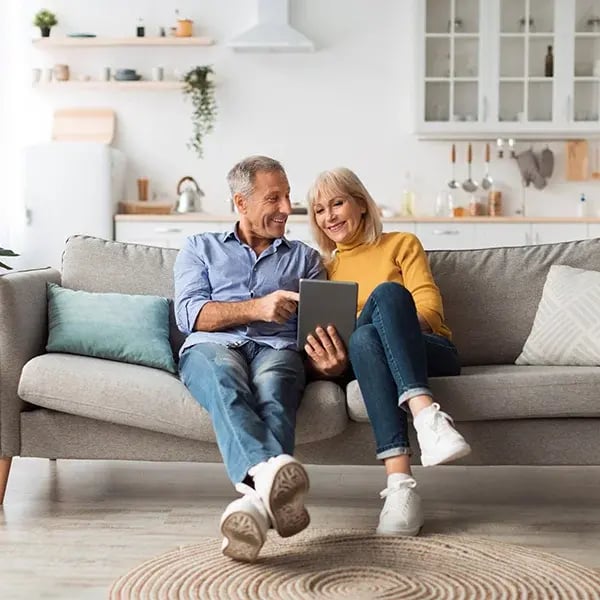 Cheerful mature spouses using digital tablet at home.