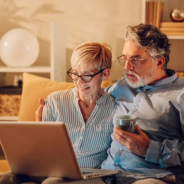 Senior couple using laptop while sitting on a couch at home.
